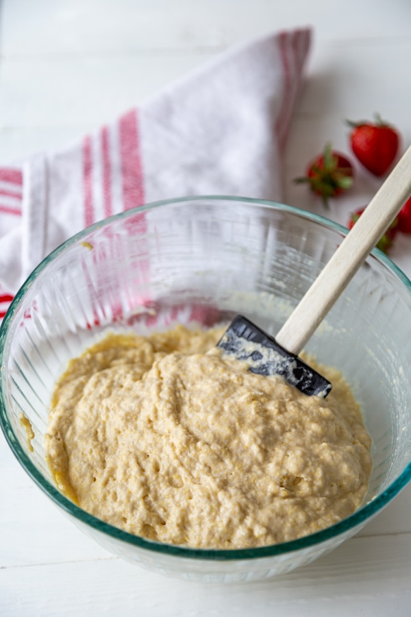 A glass bowl with a black and wood spatula stirring waffle batter.
