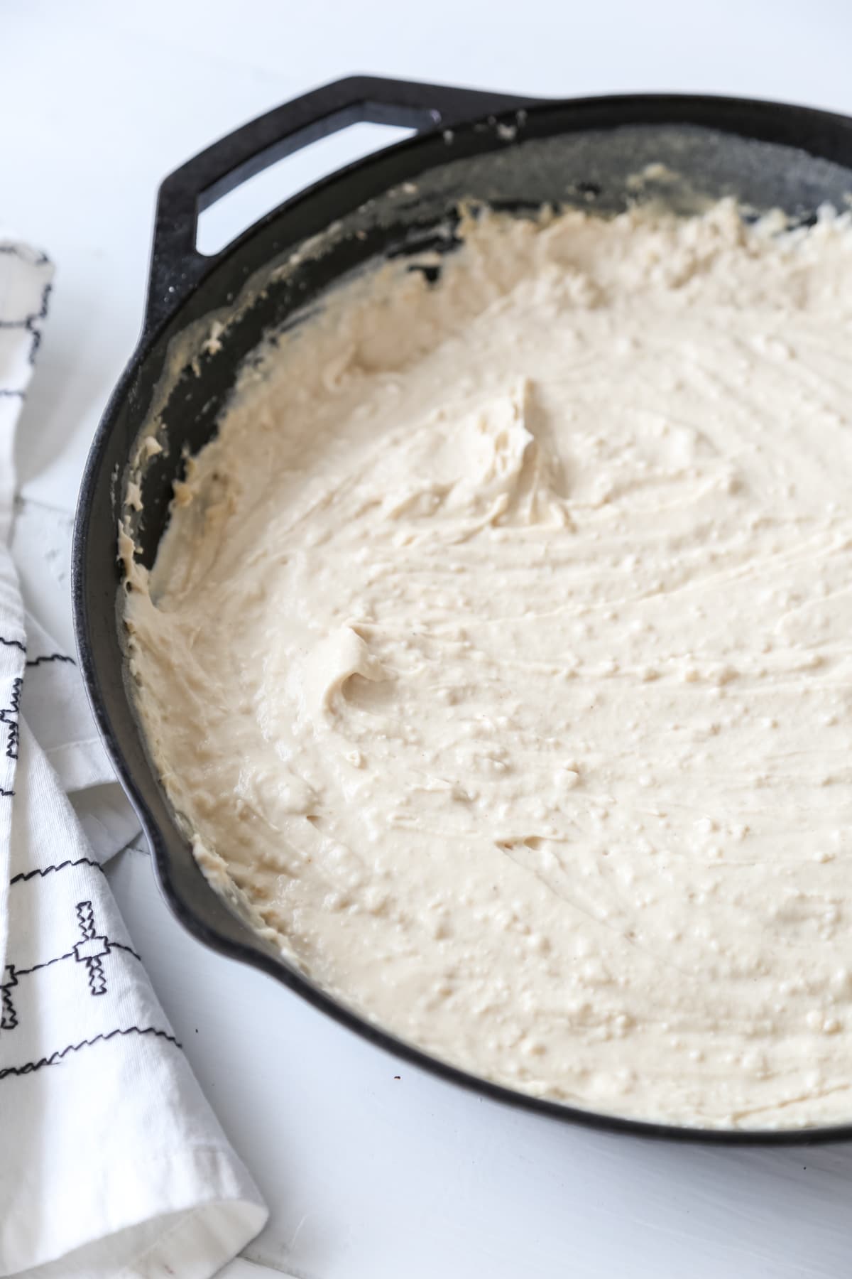 A white cream sauce in a black cast iron skillet with a white and black towel next to the pan.