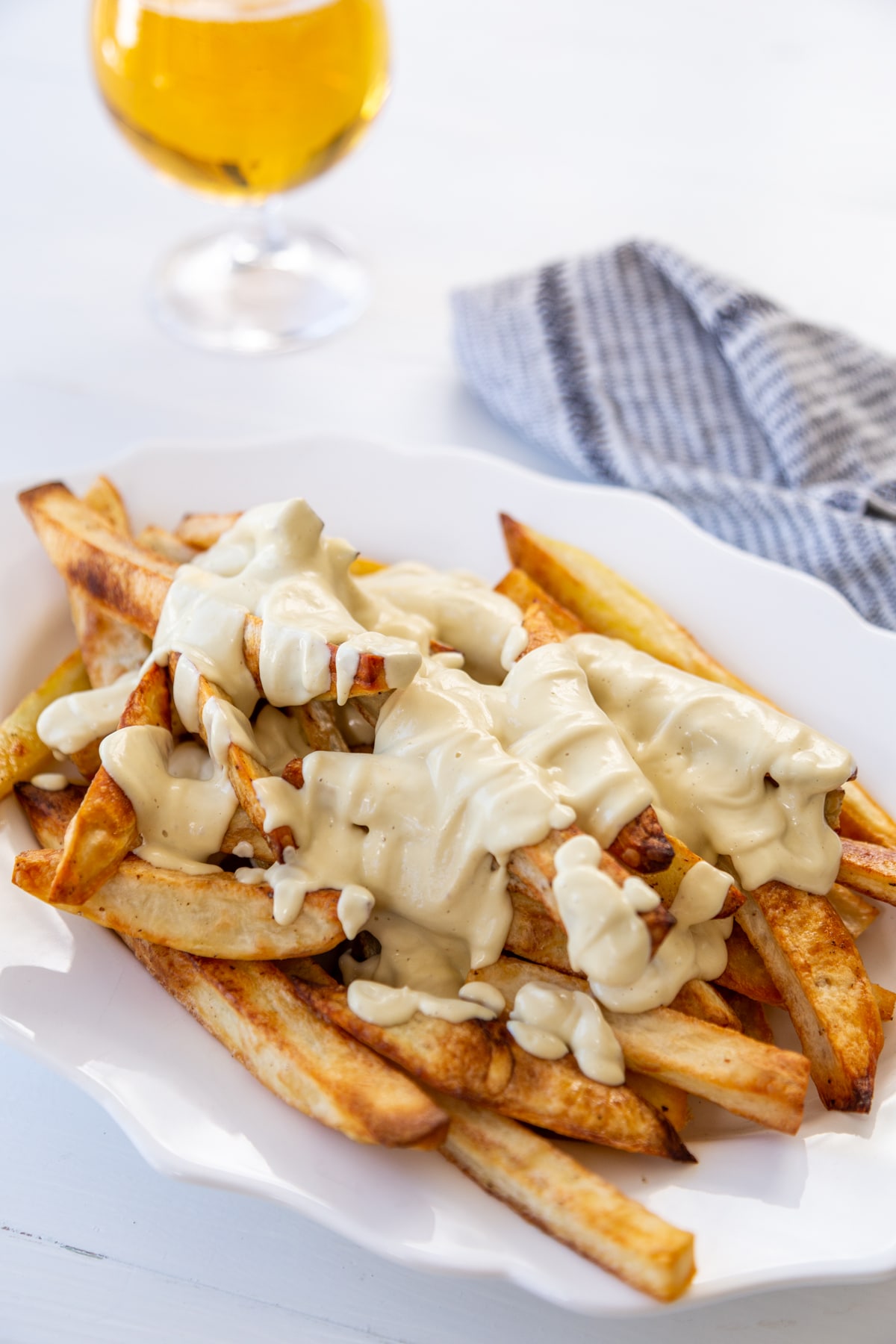 A platter of fried with cheese sauce and gravy next to a glass of beer and a black and white napkin.
