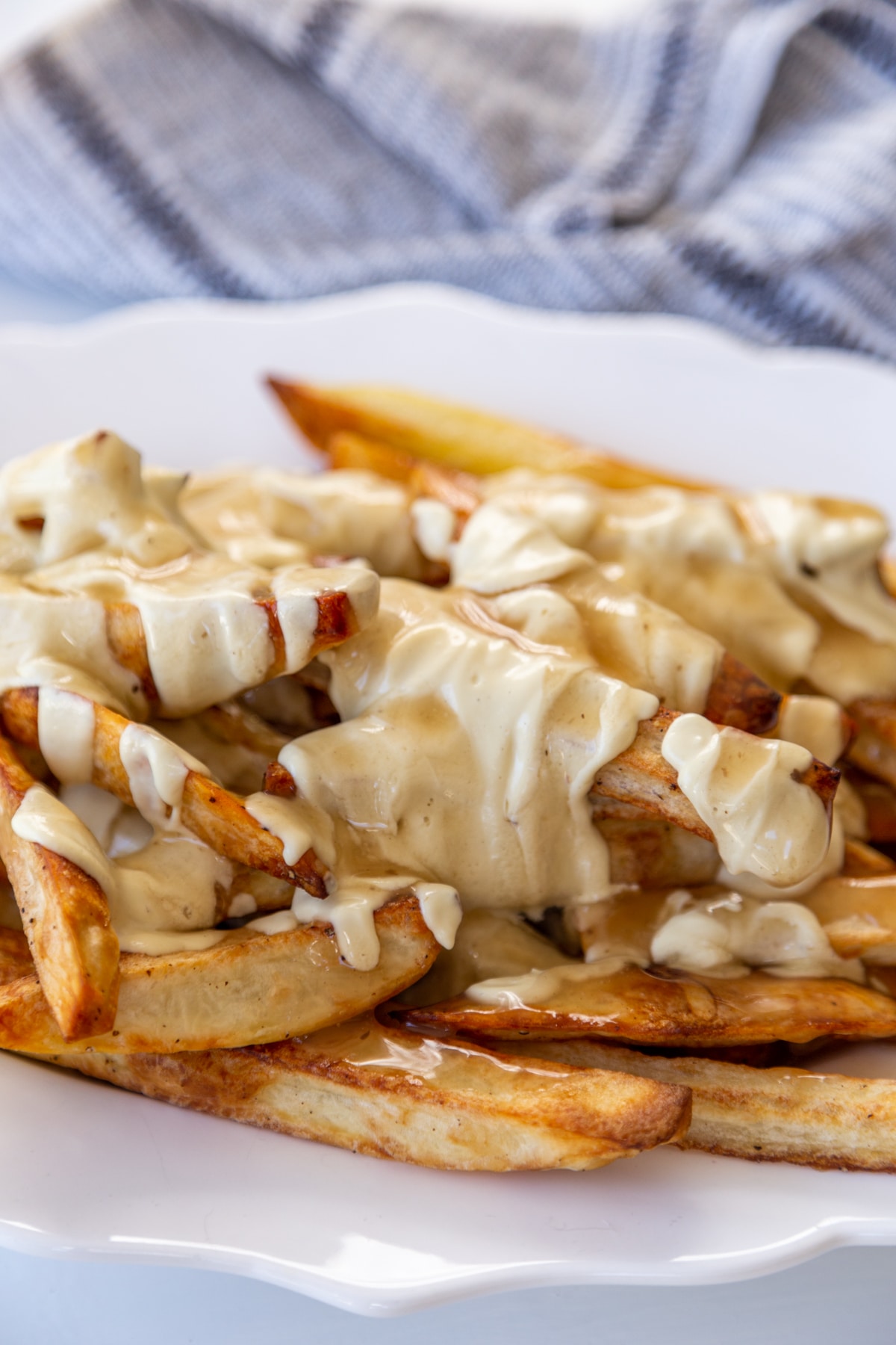 An oval white scalloped platter filled with poutine and a white and black striped towel in the background.