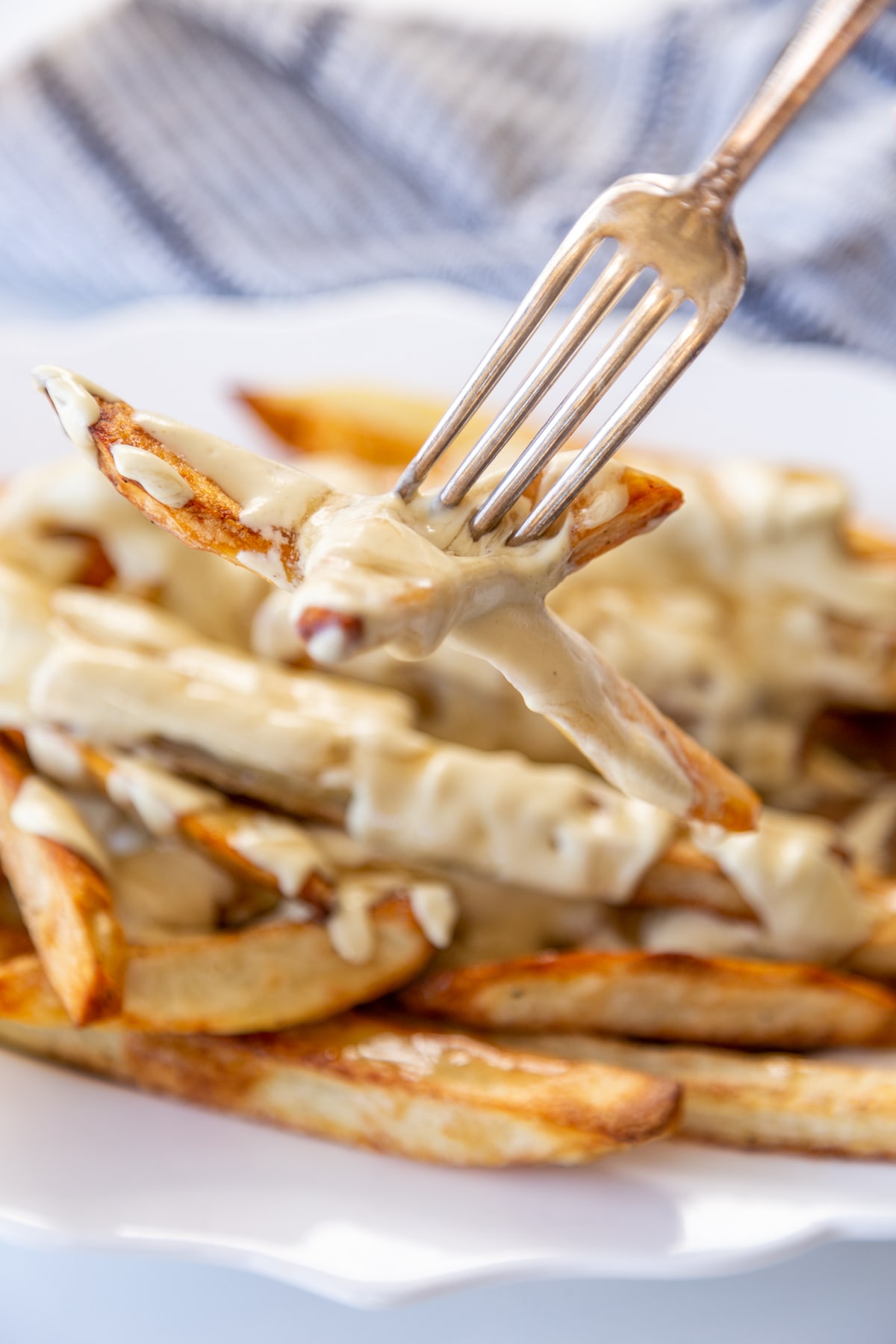 A silver fork taking a fry from a platter of poutine.
