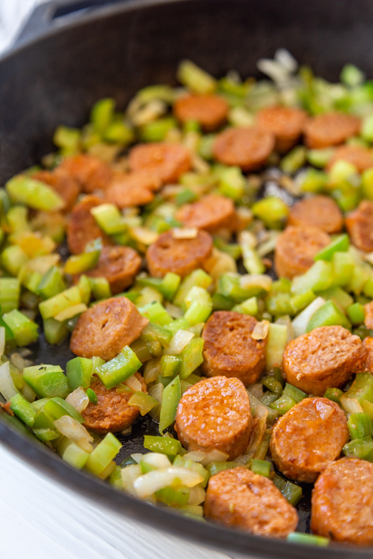 An iron skillet with onions, green bell pepper, celery, and sausage.