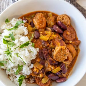 A white bowl filled with red beans and rice with sausage, and garnished with chopped parsley.