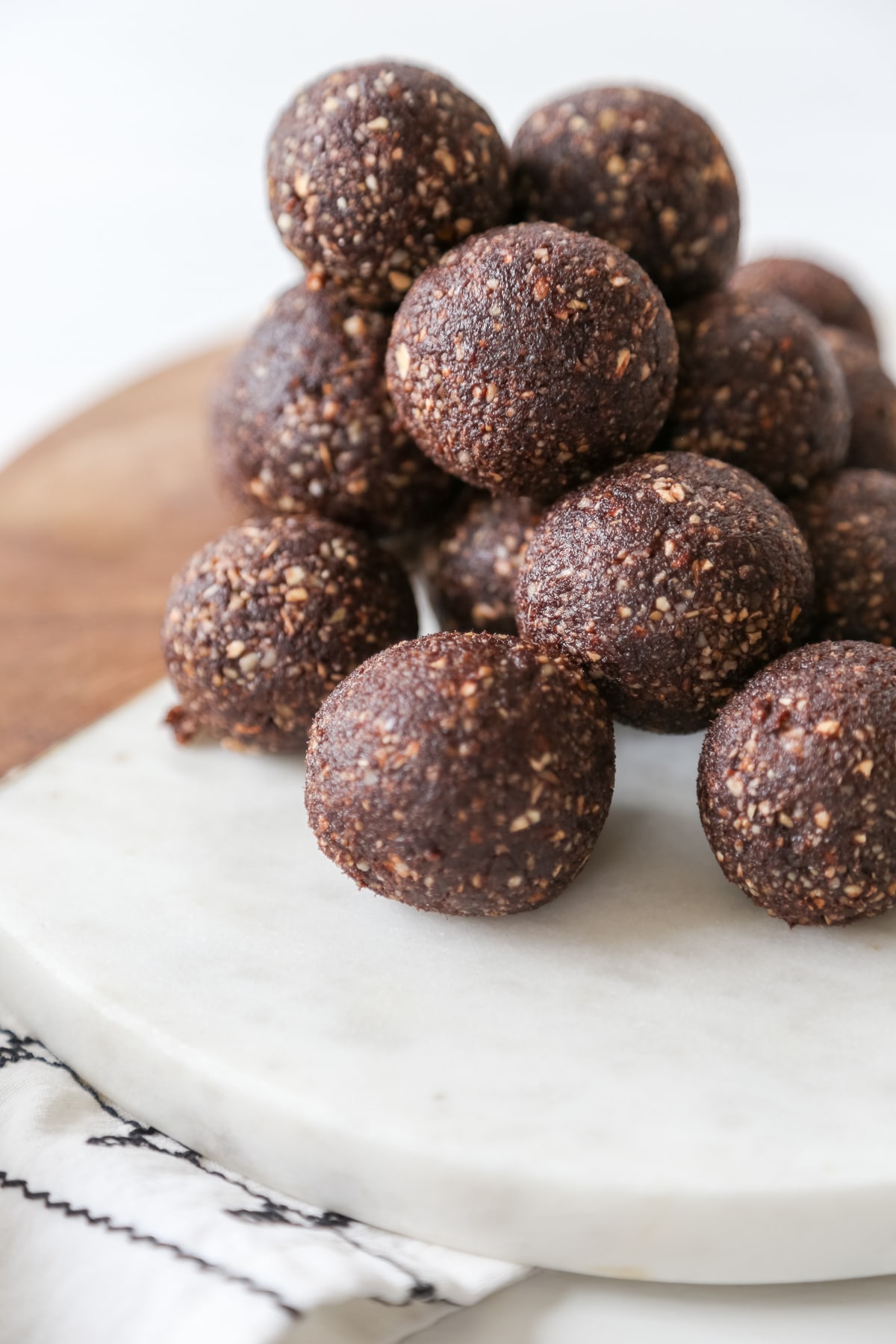 A round marble and wood board with a stack of chocolate energy balls on it.