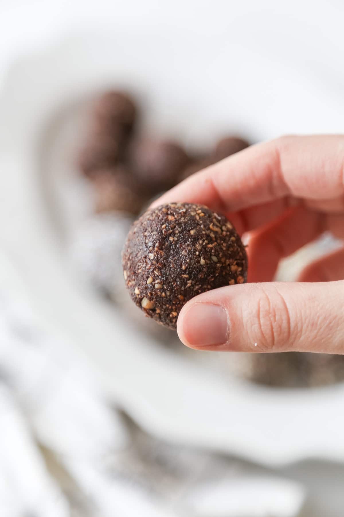 A hand holding a chocolate breakfast ball over a white platter of the balls.