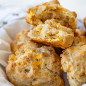 A basket of cheddar drop biscuits with the top biscuit torn in half to show the melted cheese and the texture.