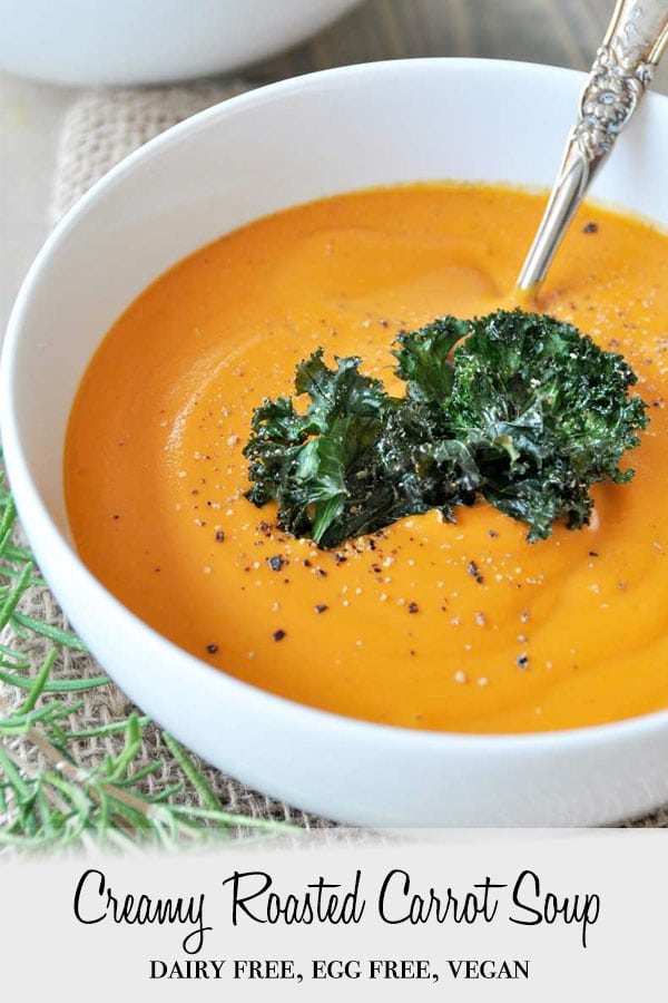 A Pinterest pin for vegan carrot soup with a picture of the soup in a white bowl with kale chips in the soup and a silver spoon.