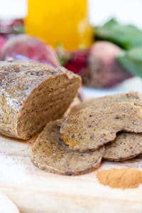 A sliced roast on a wooden board with beets in the background.