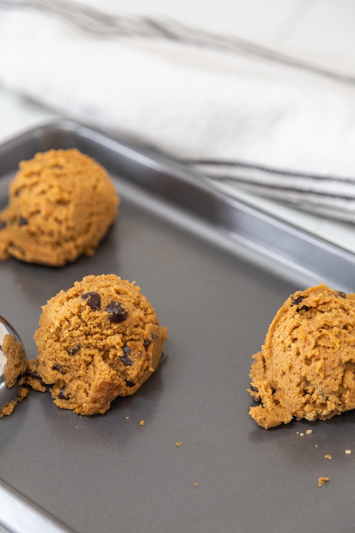 Large balls of cookie chocolate chip cookie dough on a baking sheet.