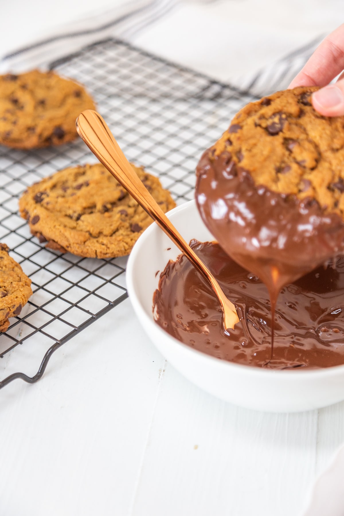 A chocolate chip cookie being dipped into a white bowl with melted chocolate.