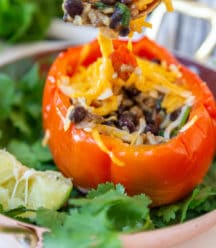 A fork with the filling from a red stuffed pepper being held over a stuffed pepper.