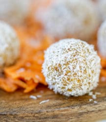 A wooden cake stand with carrot cake balls rolled in shredded coconut and shredded carrots.
