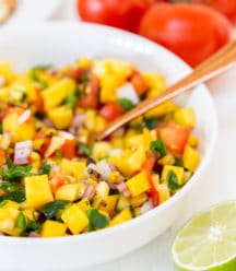A white bowl with mango salsa and a gold spoon in the bowl.